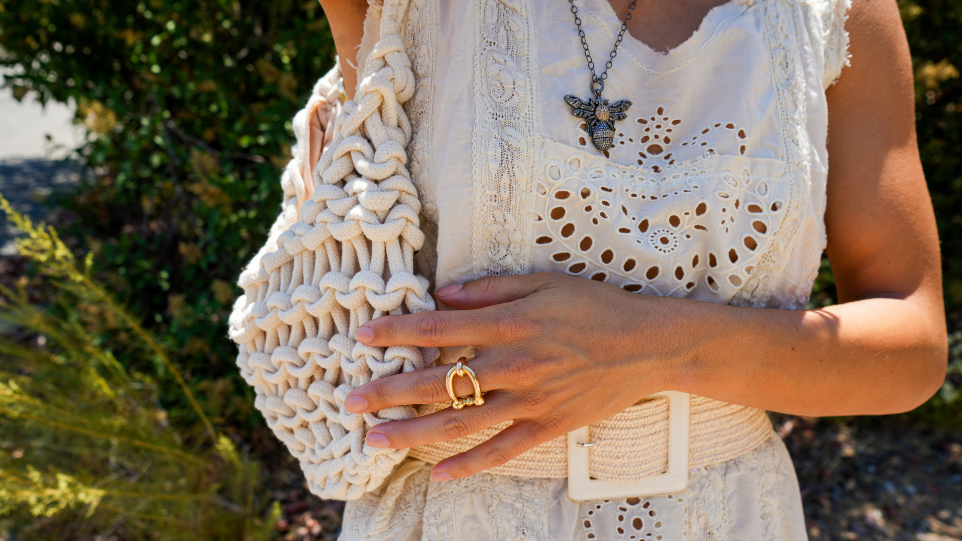 Person holding a textured beige clutch with a blurred natural background