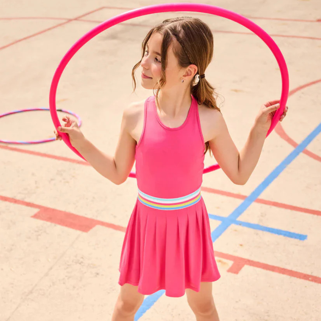 Young girl in a pink dress playing with hula hoops on a playground.
