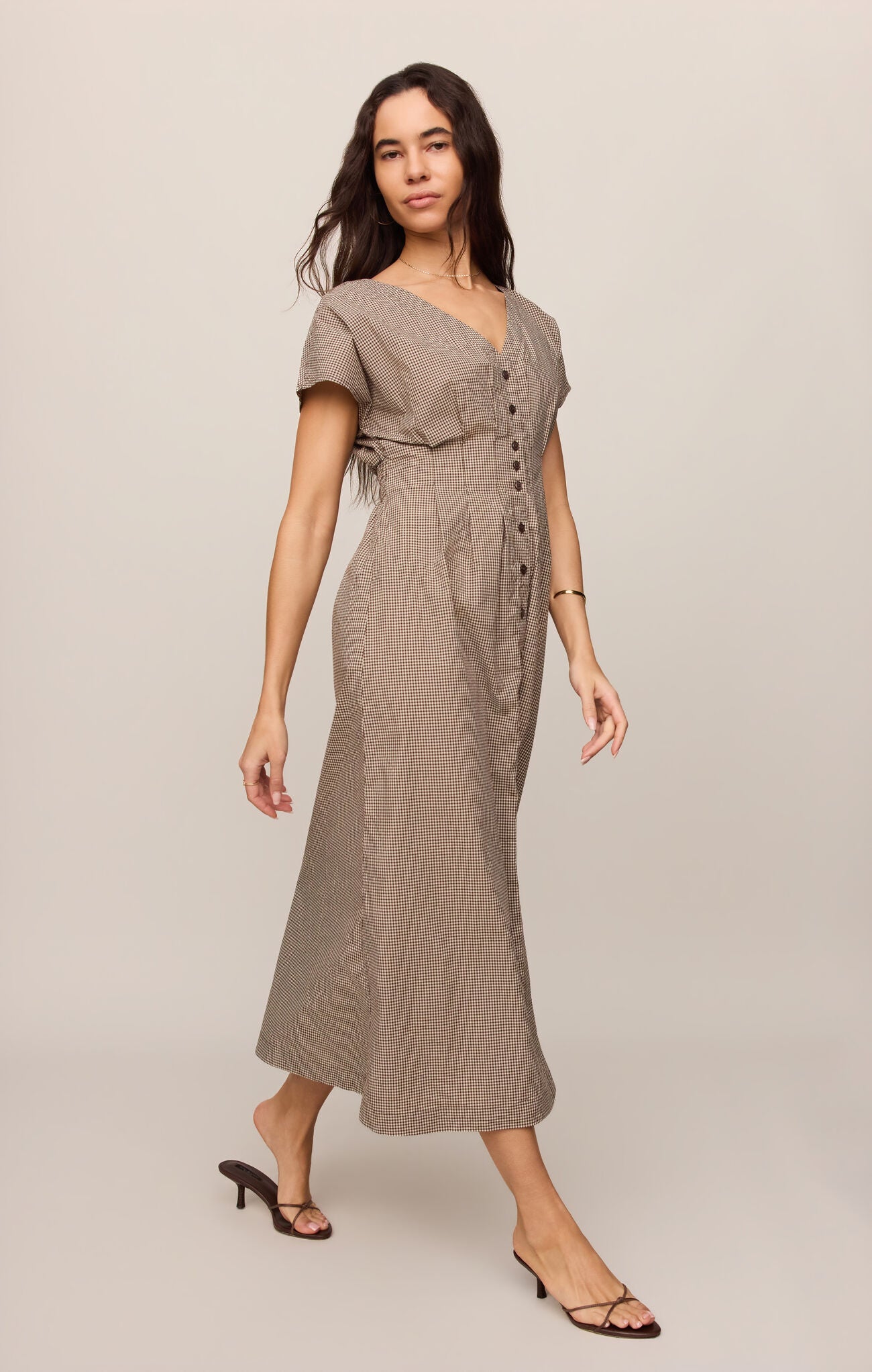 Side view of woman wearing a dark chocolate colored Sanna gingham dress against a plain background