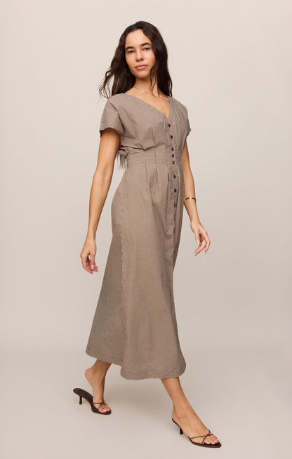 Side view of woman wearing a dark chocolate colored Sanna gingham dress against a plain background