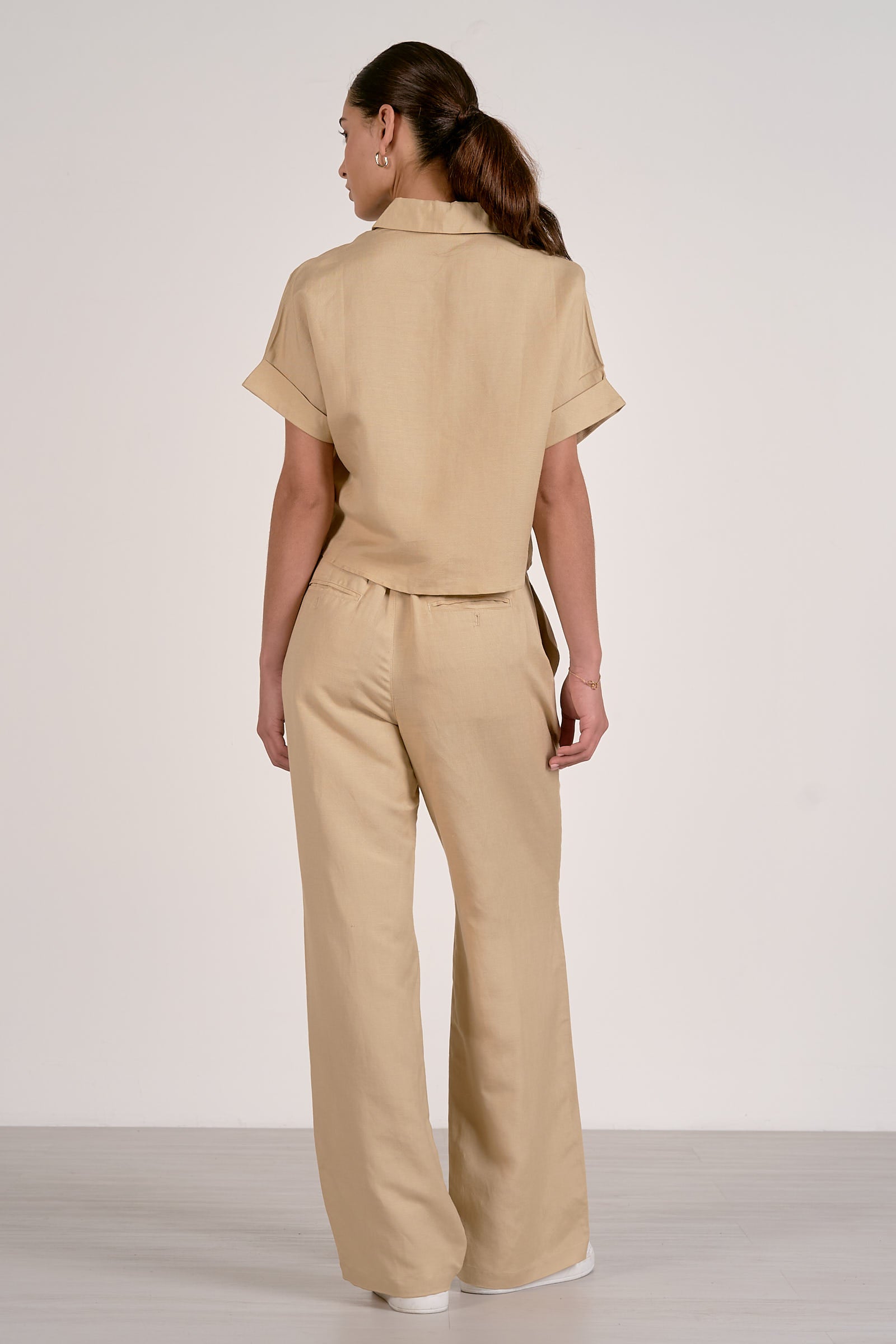 Back view of woman wearing an oatmeal shirt with a collar and wide-leg oatmeal pants on a plain background