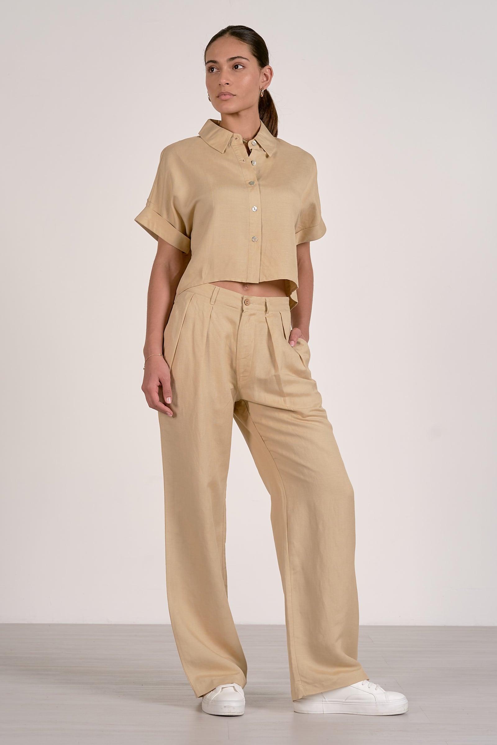 Front view of woman wearing an oatmeal button up shirt shirt and pants set on a white background