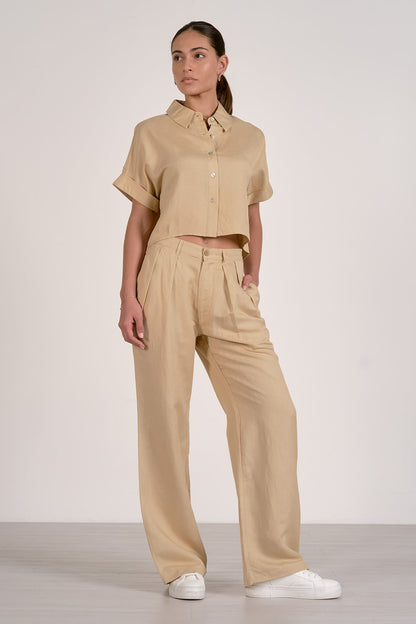 Front view of woman wearing an oatmeal button up shirt shirt and pants set on a white background