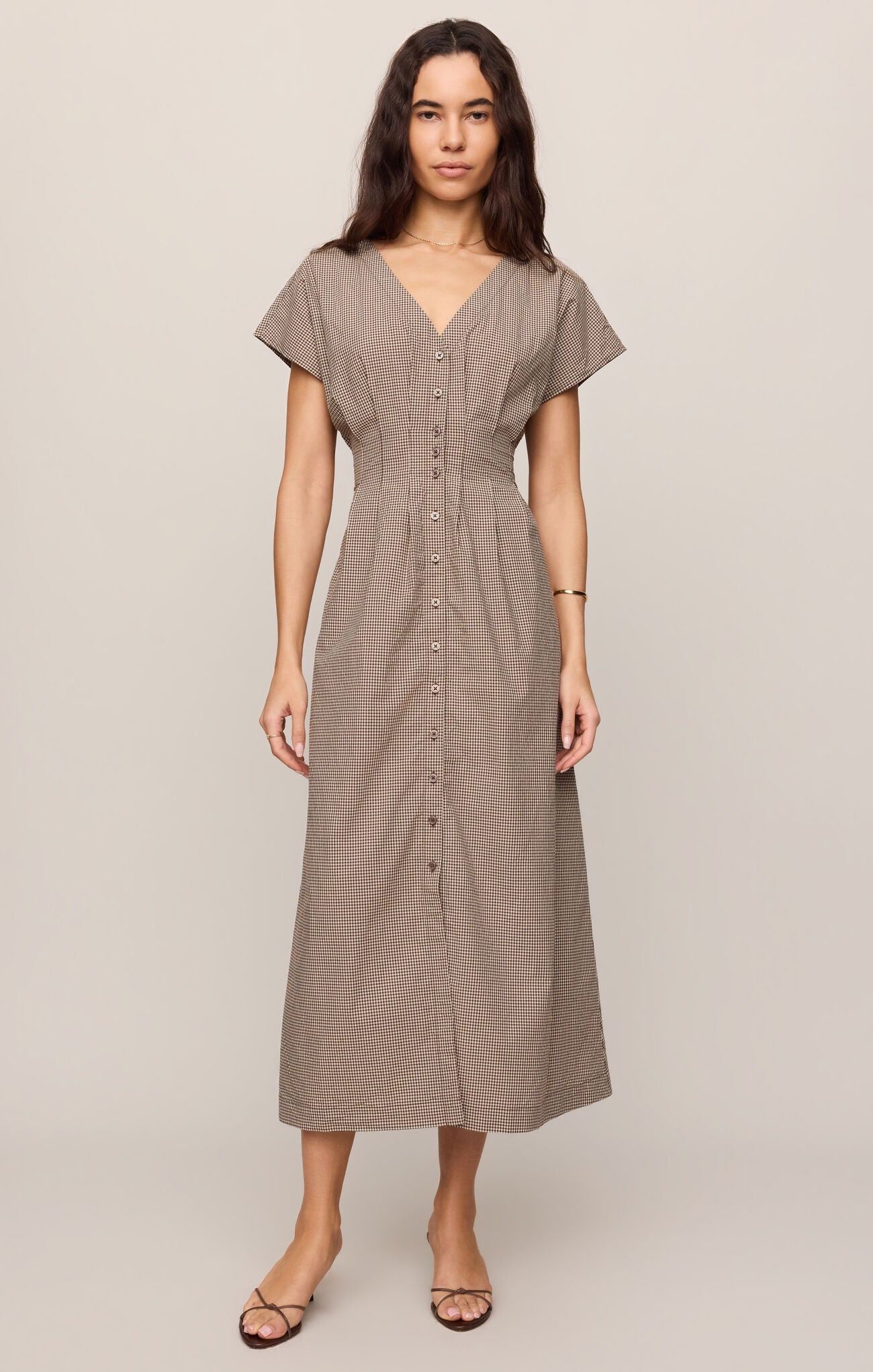 Woman wearing a dark chocolate colored sanna gingham dress against a plain background