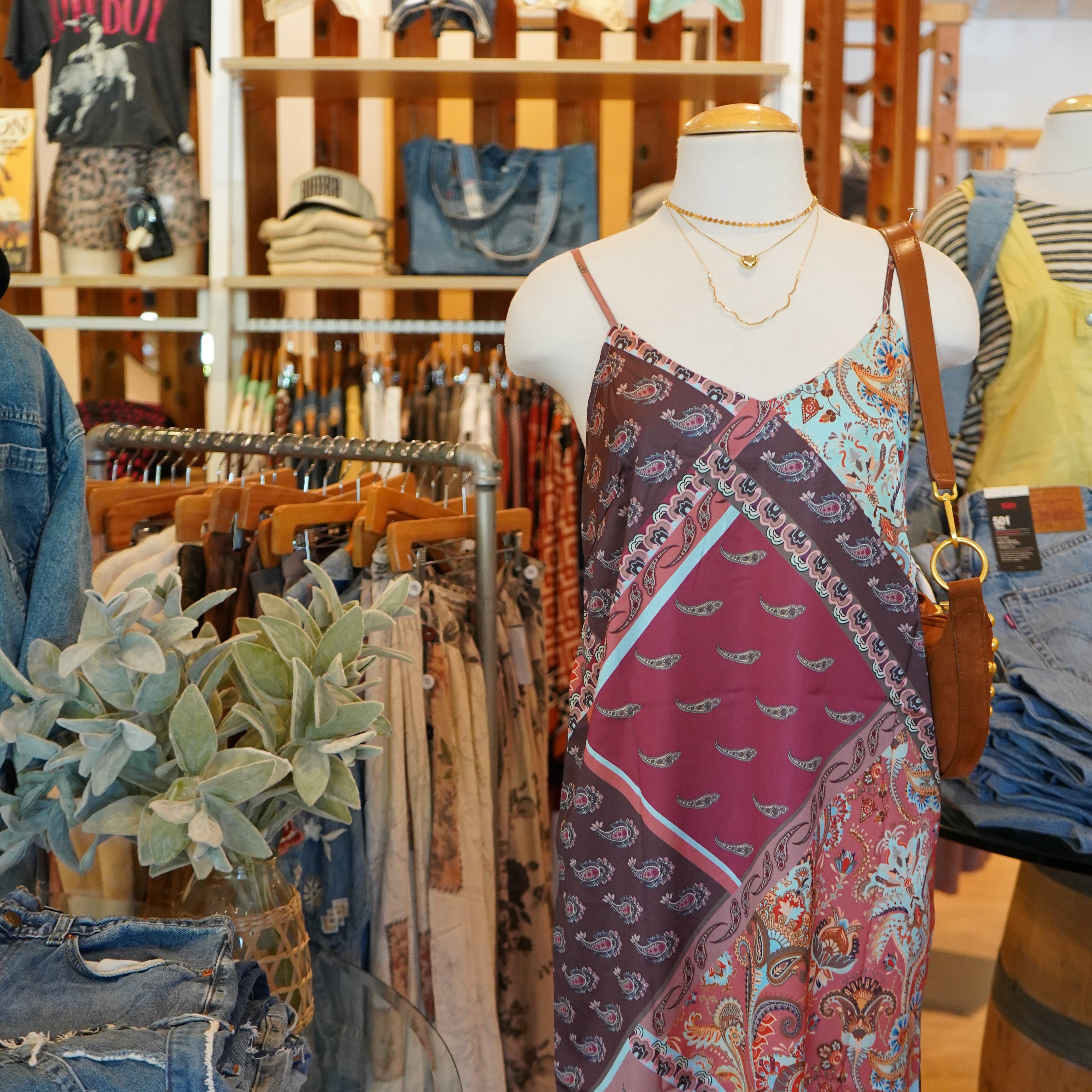 A multicolor patchwork print maxi dress with spaghetti straps and a draped silhouette, displayed on a mannequin torso inside a clothing store.