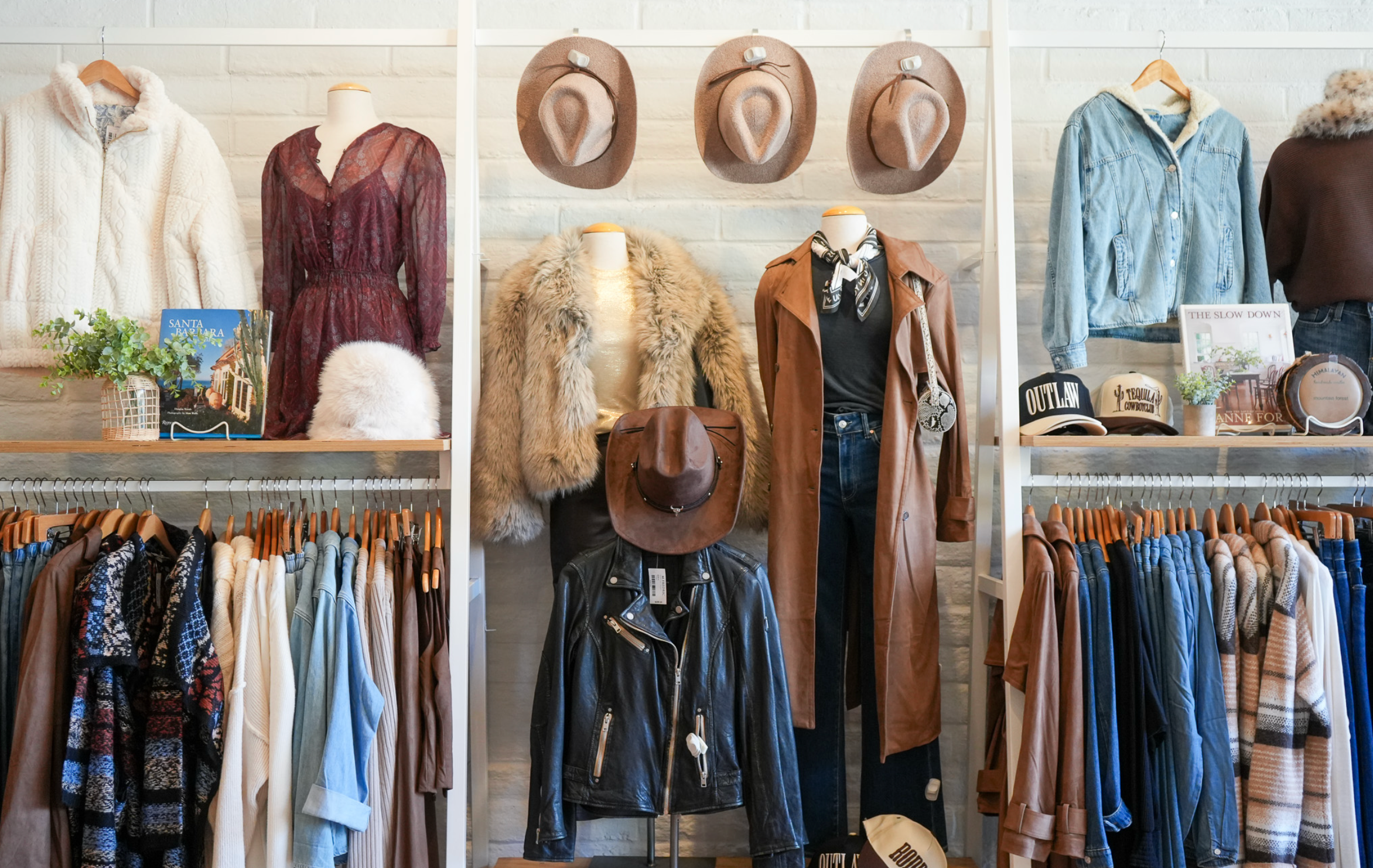 Clothing store display with jackets, hats, and pants on mannequins and racks.