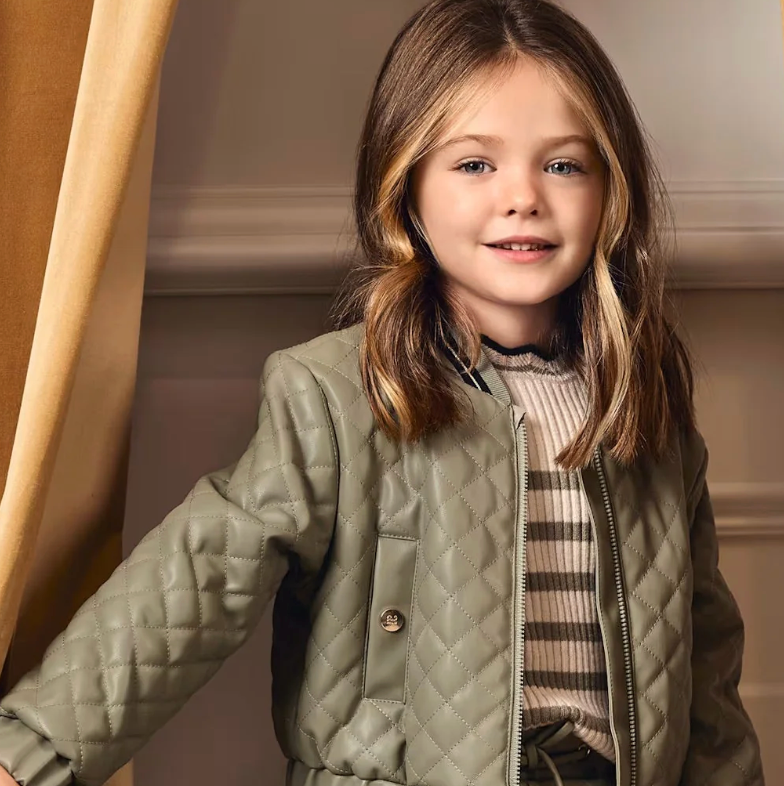 Young girl wearing a green quilted jacket indoors