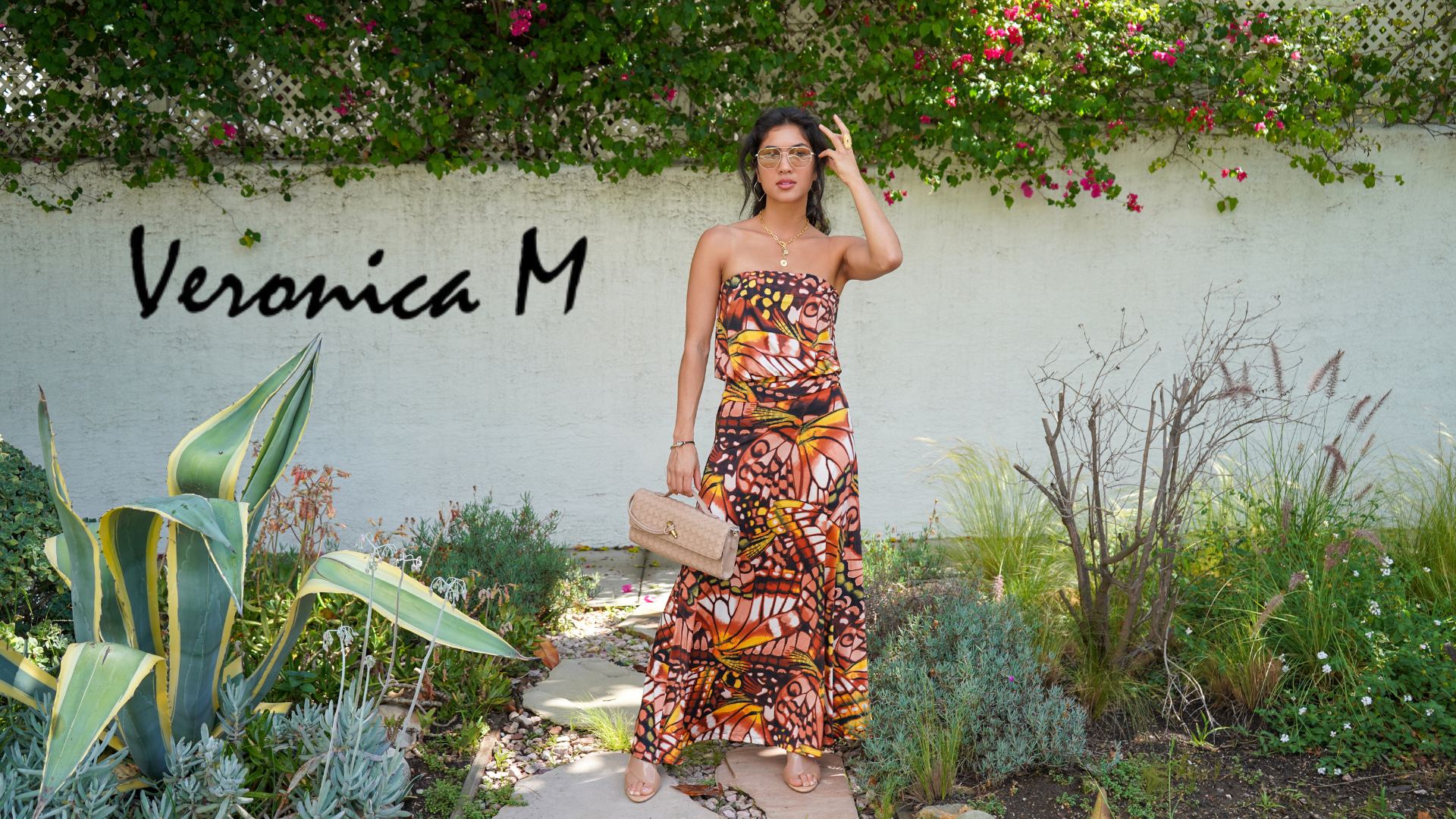 Woman in a patterned dress standing in a garden with 'Veronica M' text above.