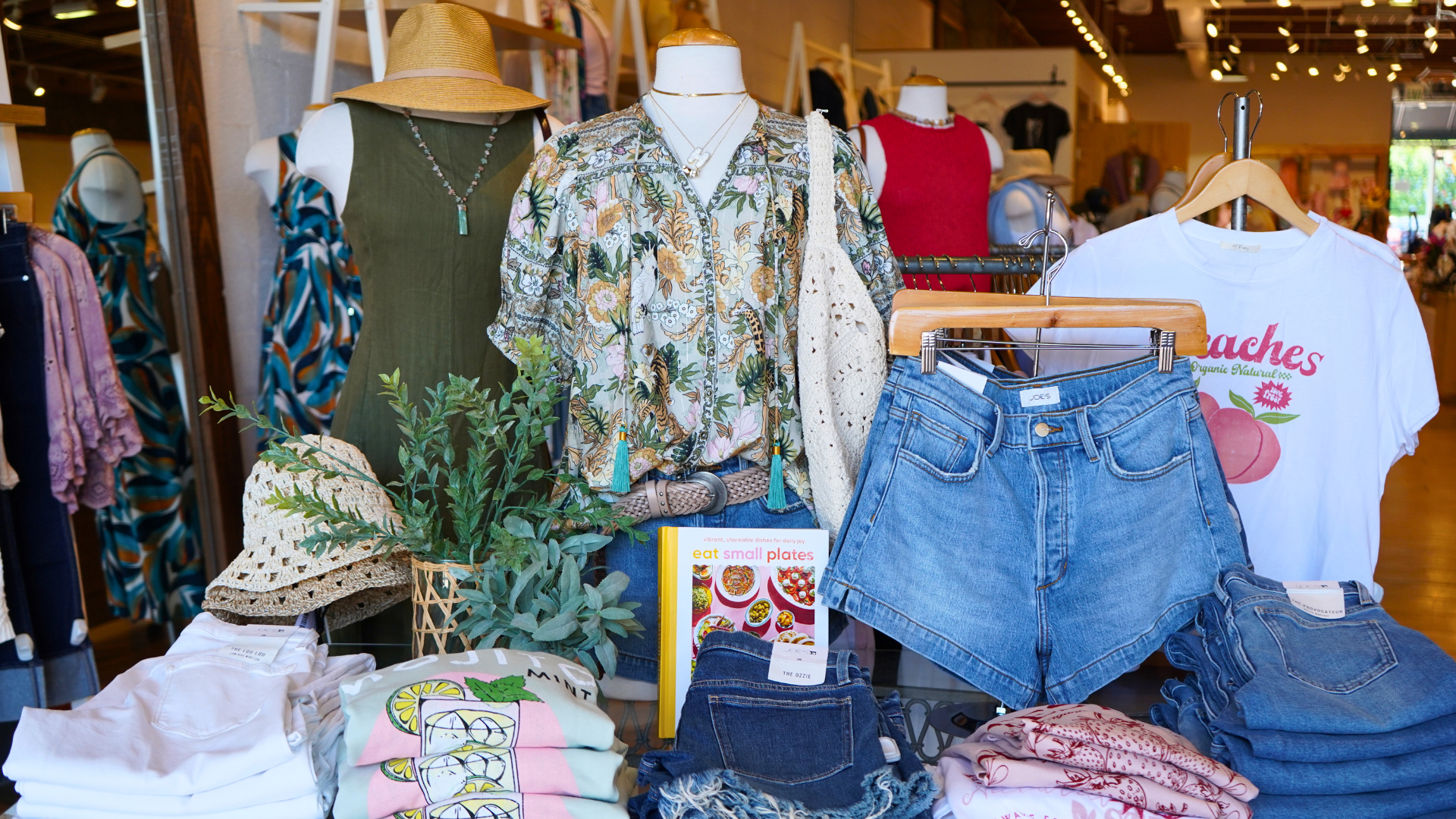 Display of clothing and accessories in a store with mannequins and racks.