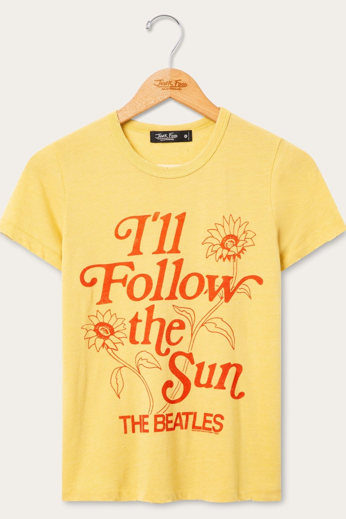 A dusty citron short-sleeve t-shirt hanging on a wooden hanger, featuring a retro-style red graphic print that reads 'I'll Follow the Sun' with sunflower illustrations and 'THE BEATLES' text.
