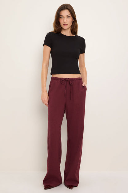 A woman modeling a black short-sleeve crop top and port royale burgundy wide-leg drawstring pants against a plain off-white studio background.