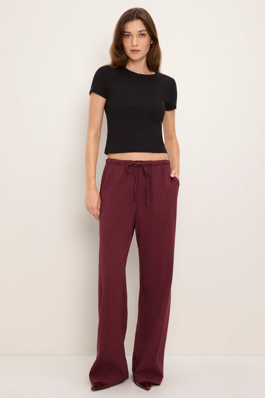 A woman modeling a black short-sleeve crop top and port royale burgundy wide-leg drawstring pants against a plain off-white studio background.