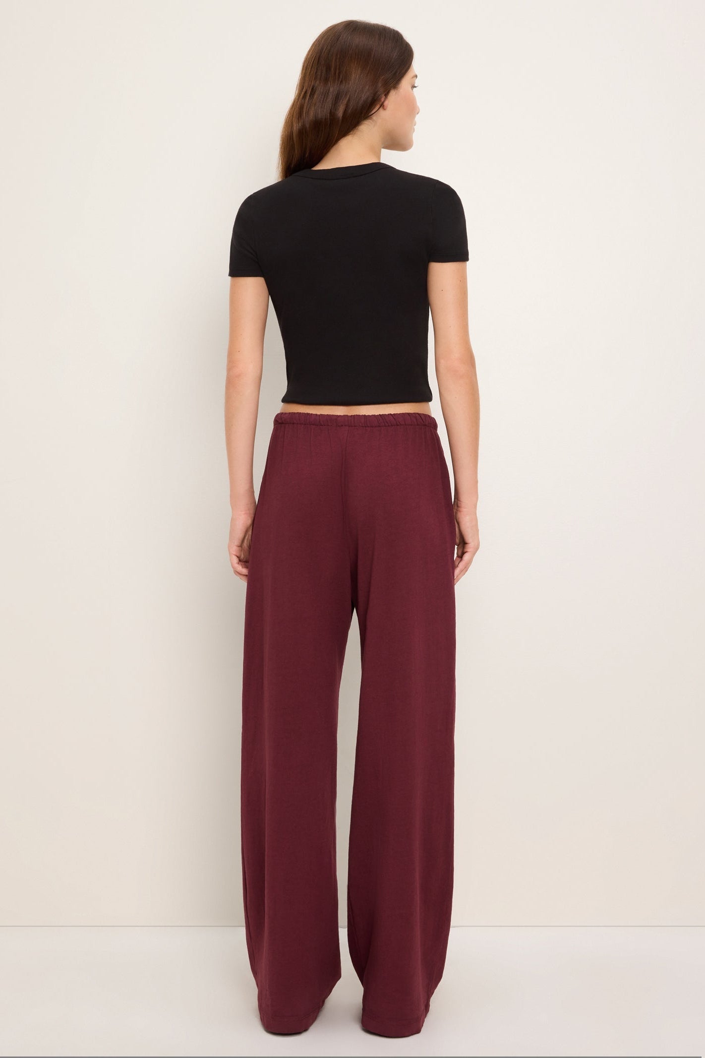 A woman shown from the back wearing a black short-sleeve crop top and 'port royale' burgundy wide-leg pants, standing against a plain off-white studio background.