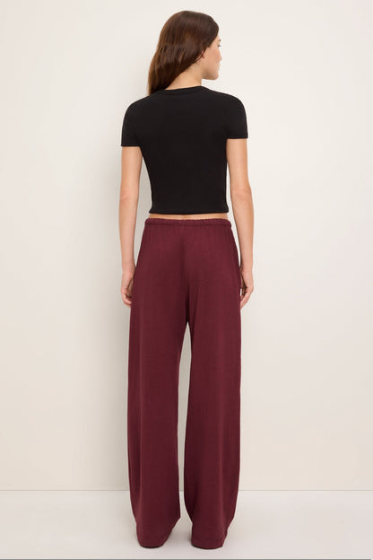 A woman shown from the back wearing a black short-sleeve crop top and 'port royale' burgundy wide-leg pants, standing against a plain off-white studio background.