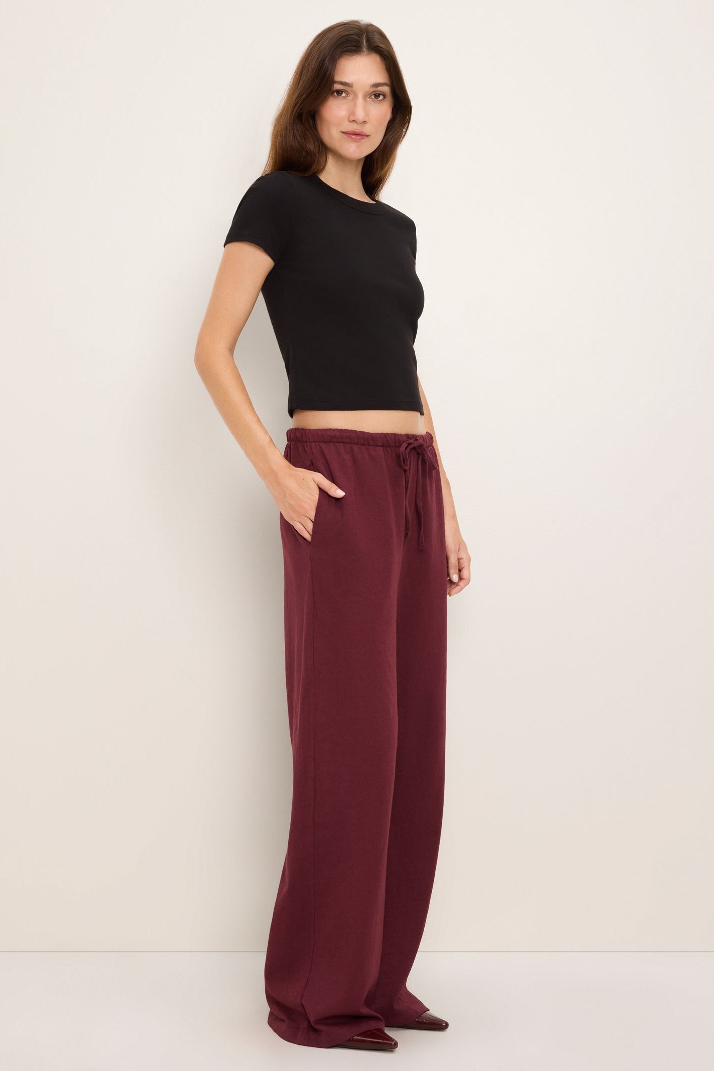 A woman modeling a black short-sleeve crop top and 'port royale' burgundy wide-leg drawstring pants against a plain off-white studio background.