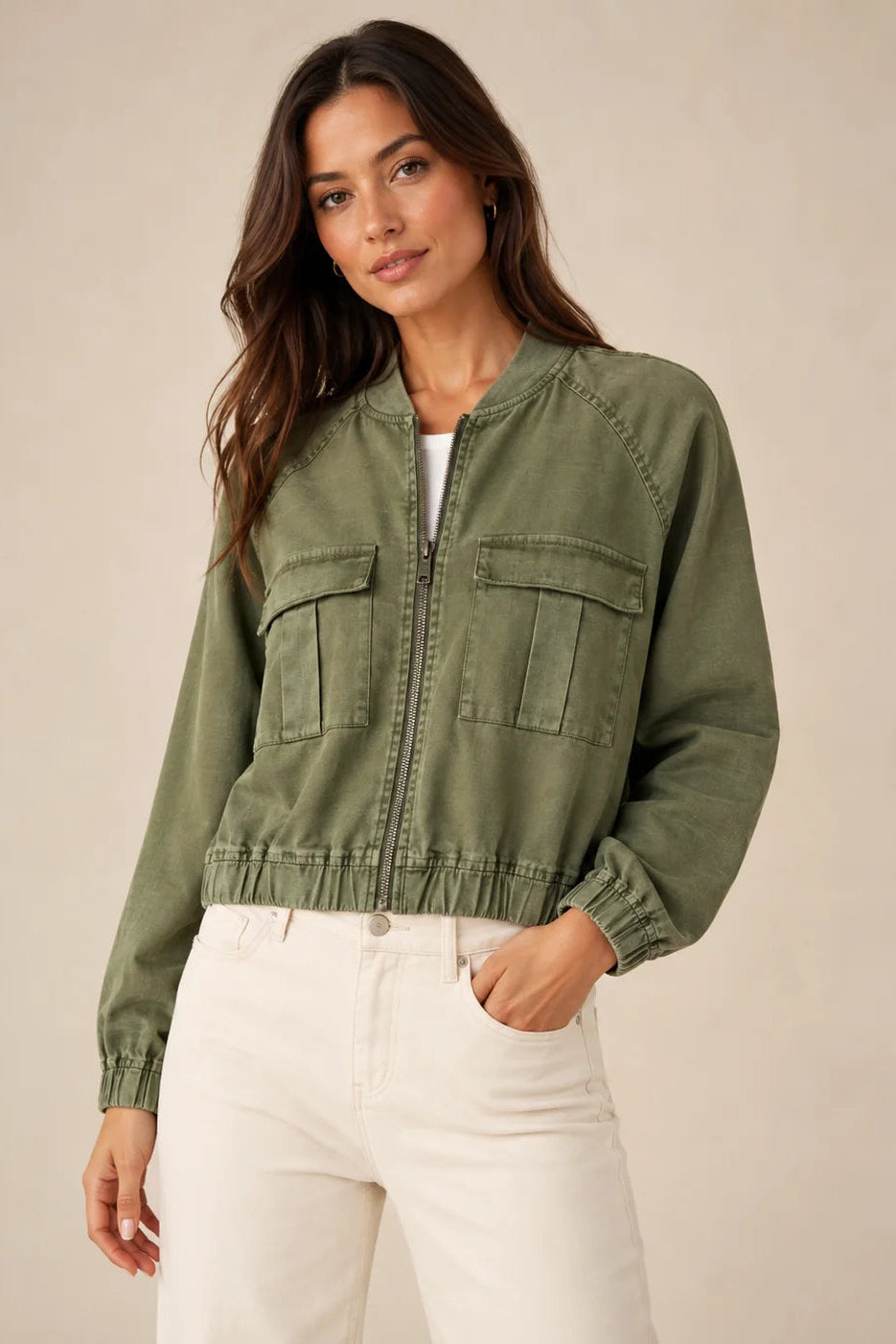 Woman wearing alex bomber jacket with zip front in avocado green color with white pants