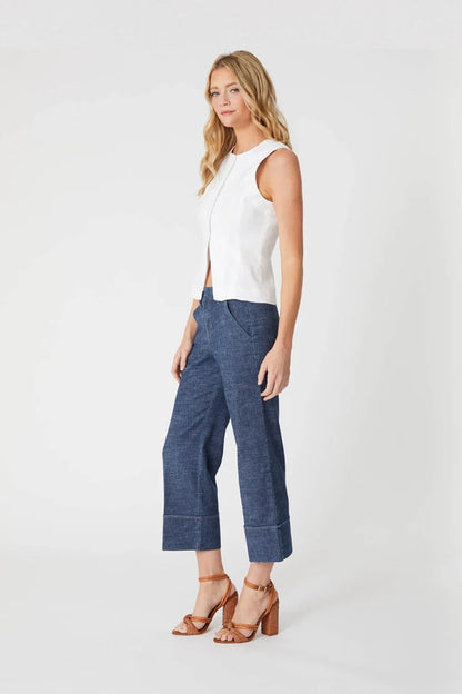 A woman modeling a sleeveless white top and blue cropped wide-leg pLauren Cuffed Trousers with brown heeled sandals, photographed against a clean light gray studio background.